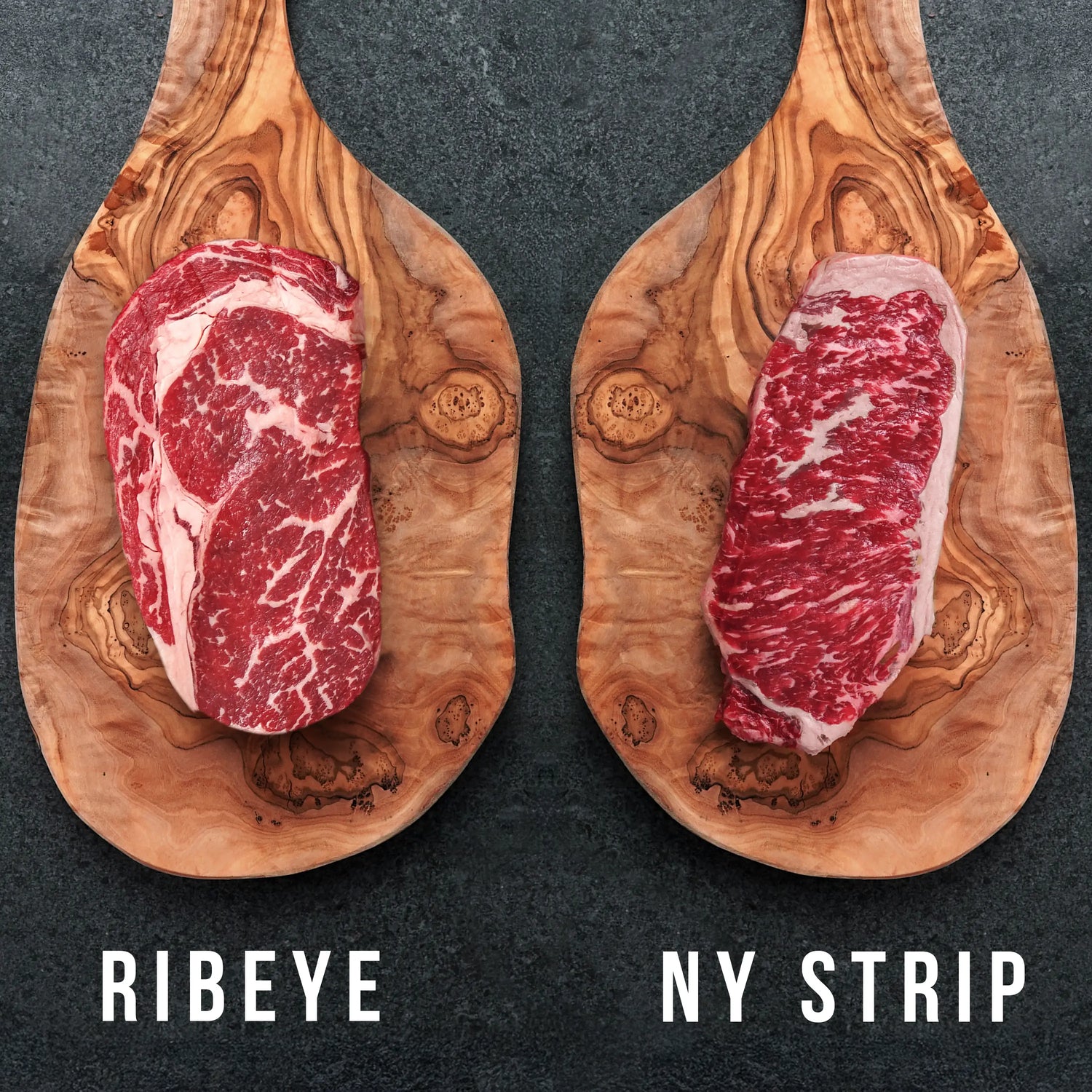 raw steaks on wood boards wth words ribeye and NY strip below on dark surface