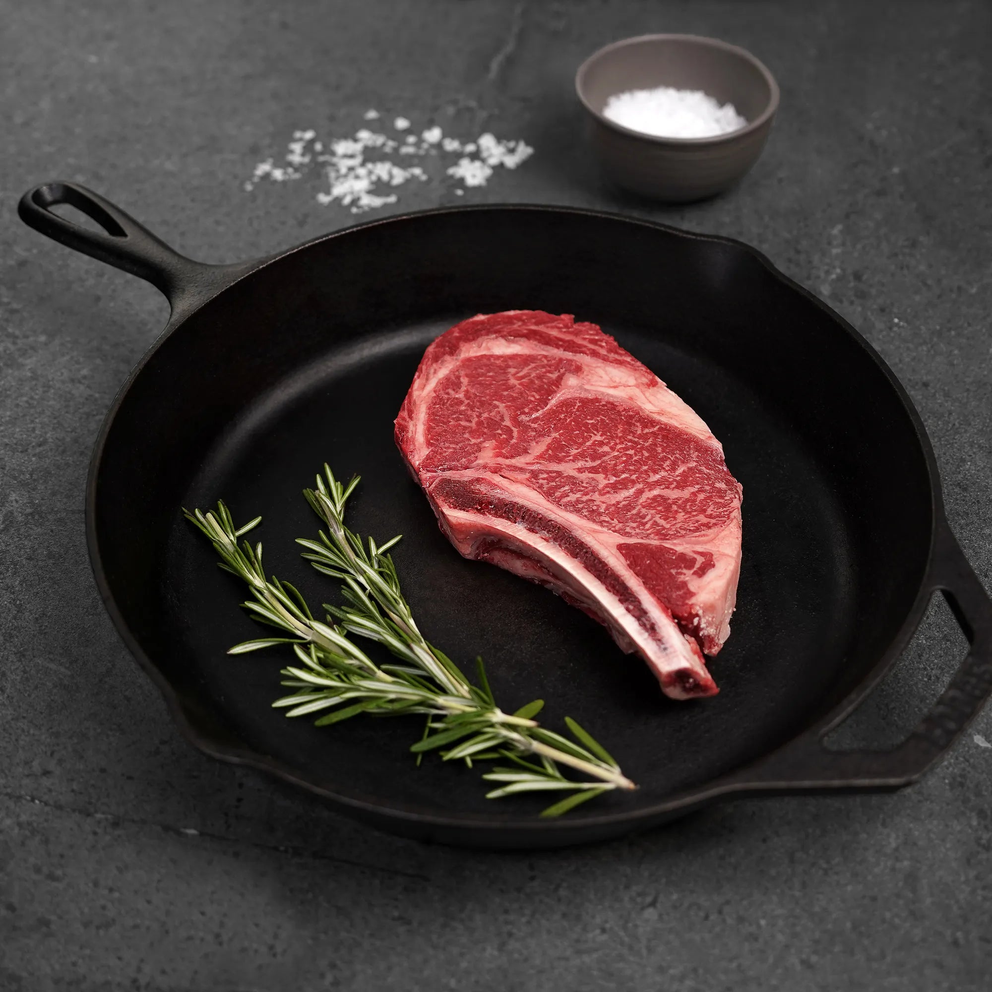 raw bone in ribeye steak on cast iron pan with green garnish