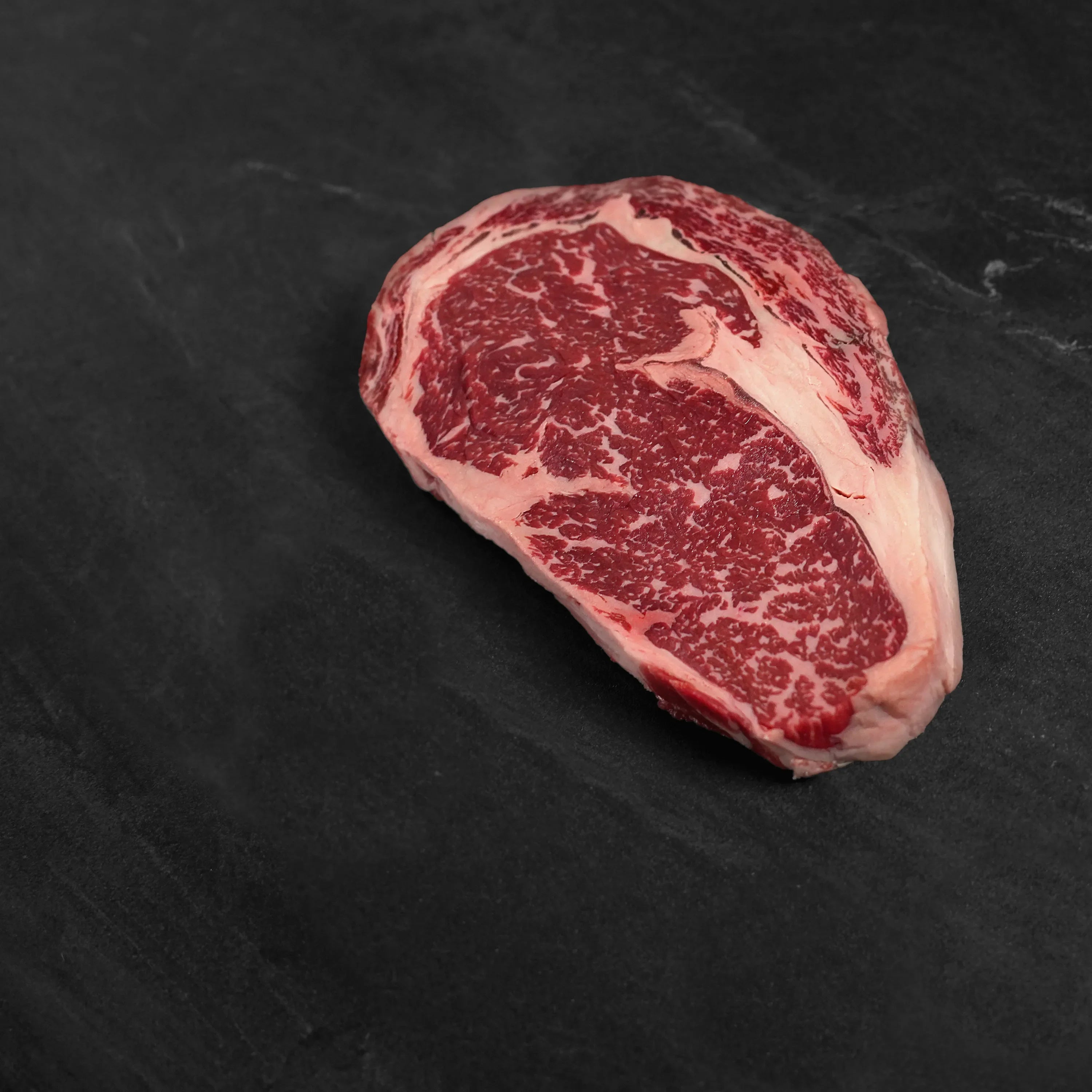 raw boneless ribeye steak on dark surface