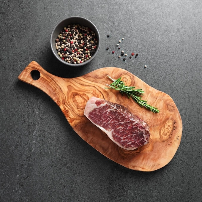 raw steak on wood board with whole peppercorn and rosemary garnish