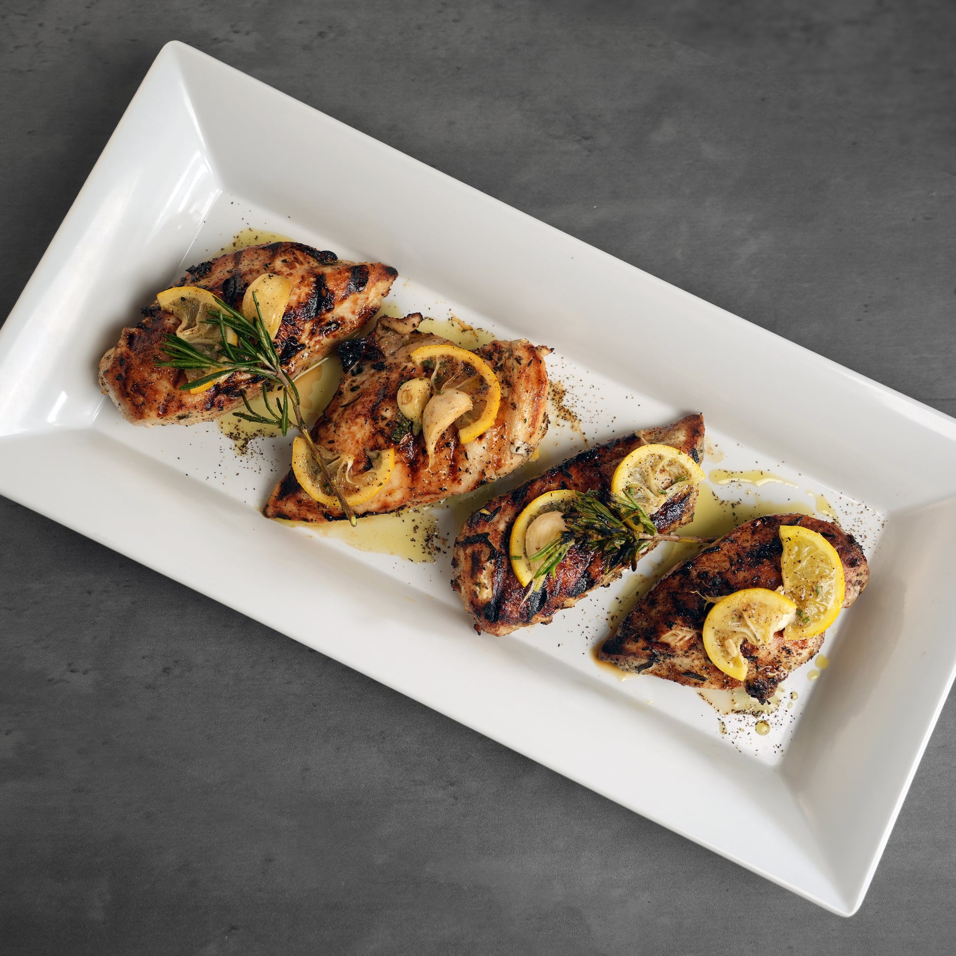 Allen Brothers cooked organic boneless skinless chicken breast topped with lemons on a white plate