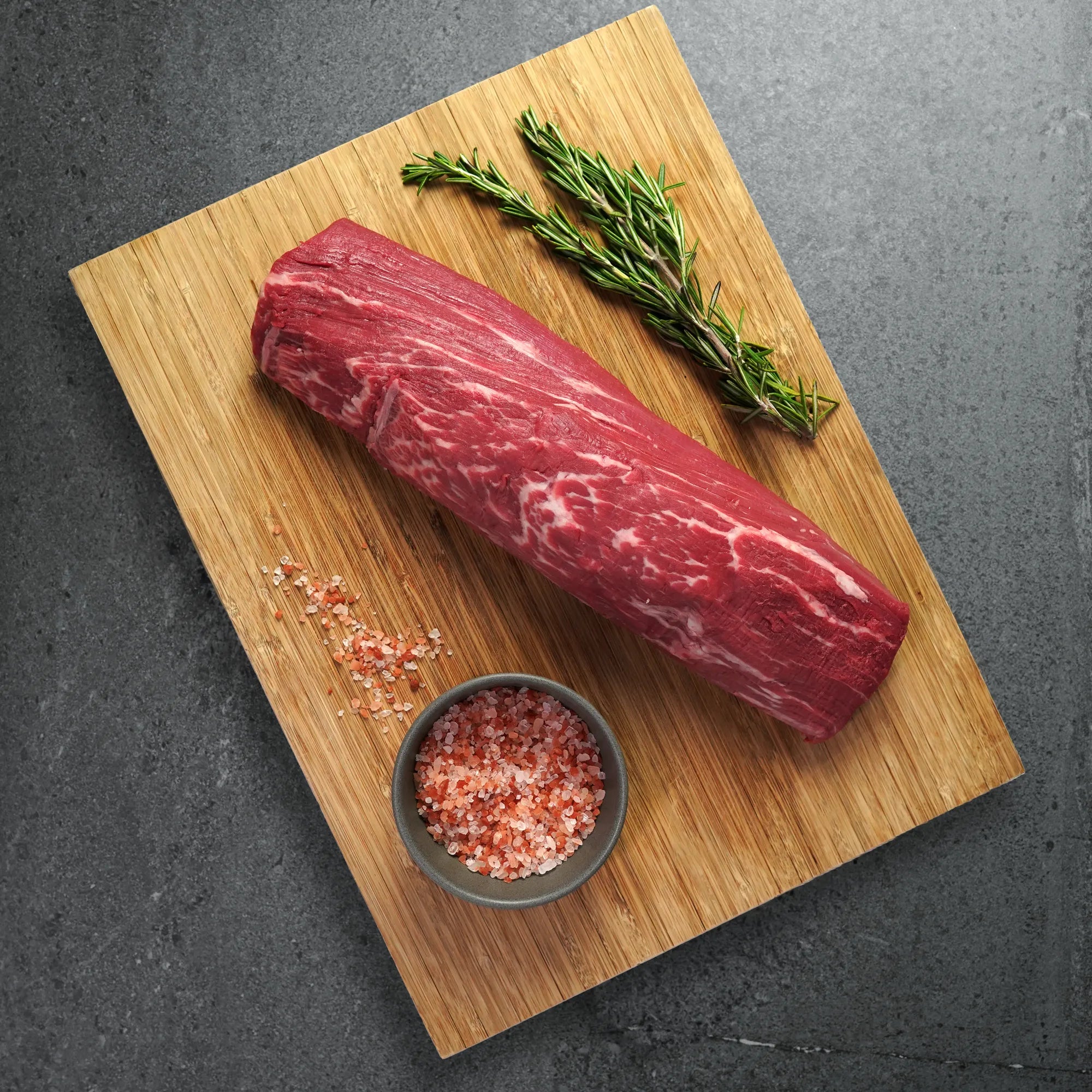 Raw steak on wood board with rosemary garnish