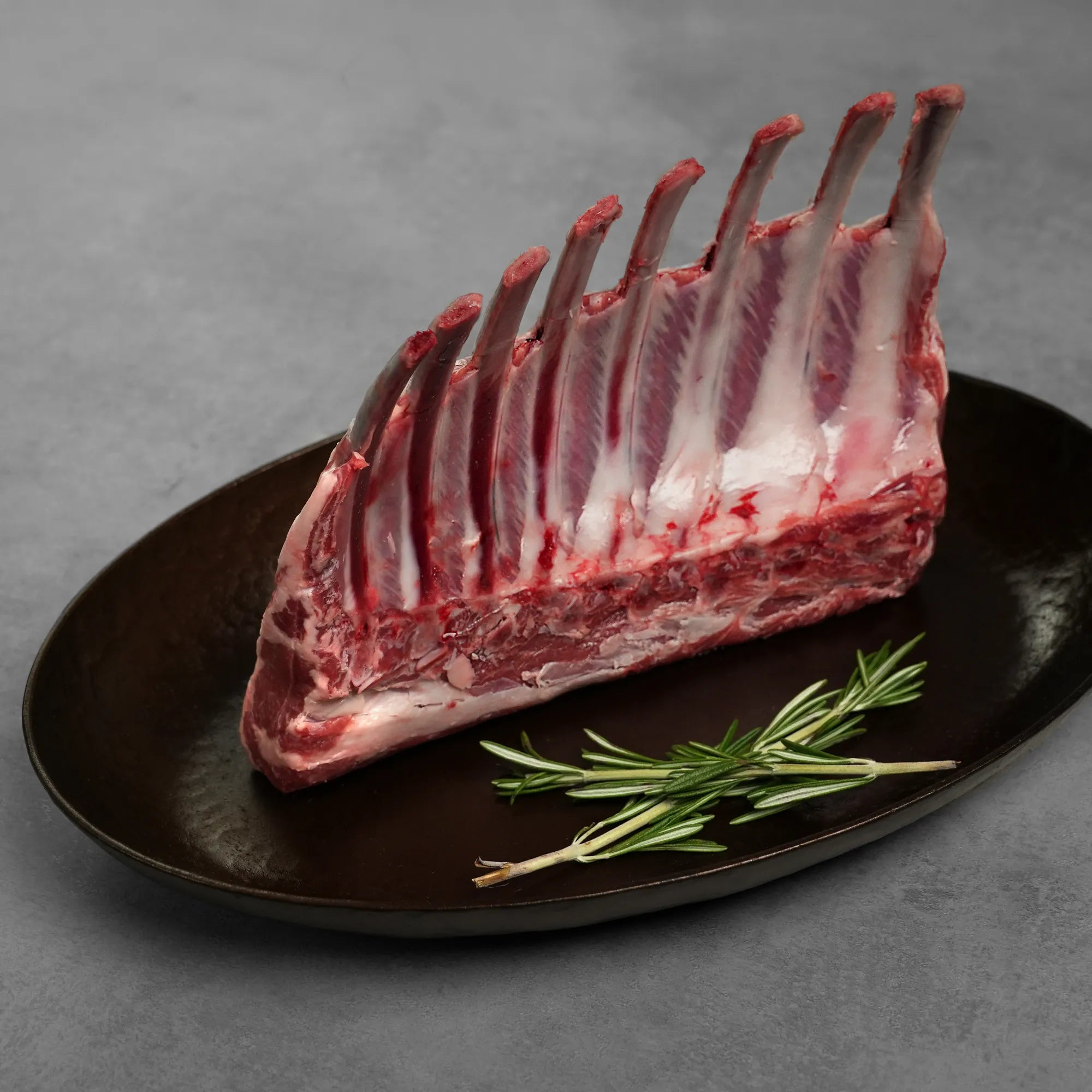 Allen Brothers Domestic all natural rack of lamb raw standing on a black plate with rosemary
