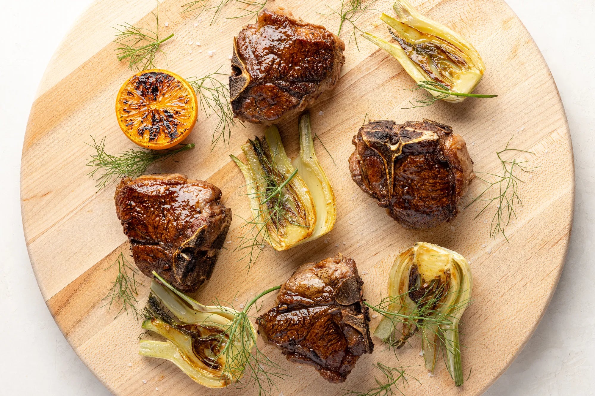 Allen Brothers Domestic All Natural Lamb Loin T-Bone Chop Cooked on circular wooden board with garnishes