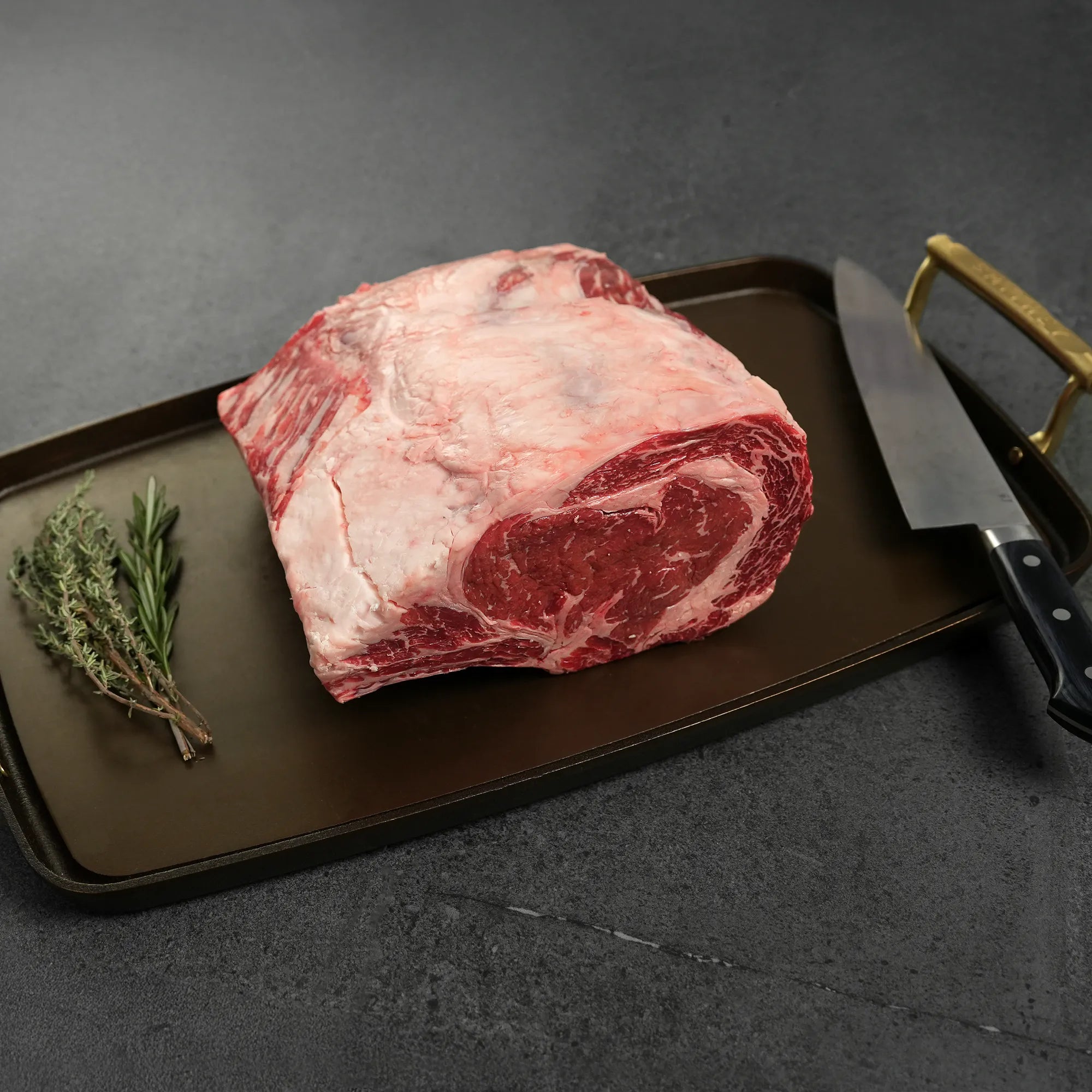 Raw meat on metal pan with gold handles and rosemary garnish