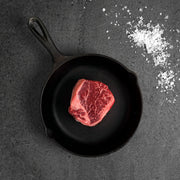 Raw steak in a cast iron skillet on a dark surface with salt crystals.