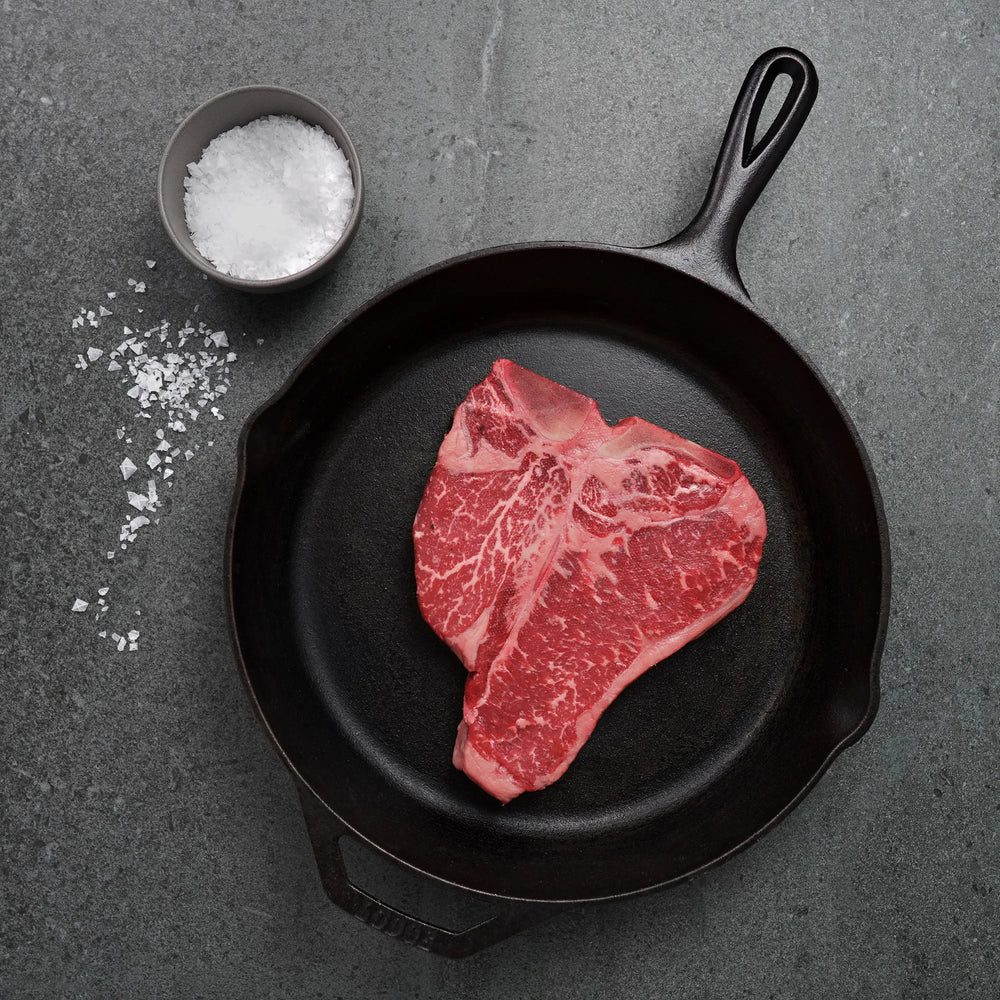 Raw steak on black iron pan with salt in container on the side
