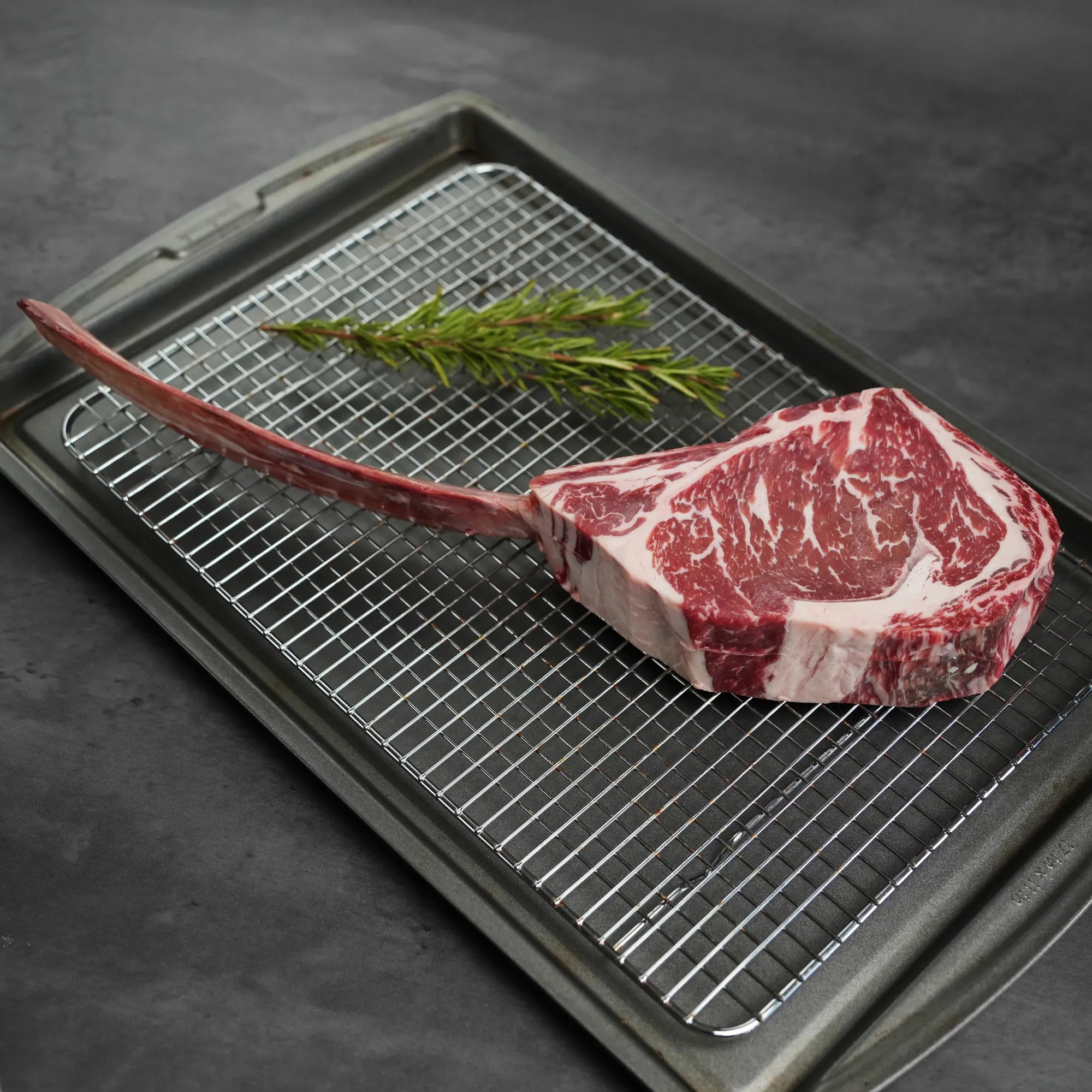 Raw ribeye steak on a grill pan with a sprig of rosemary.
