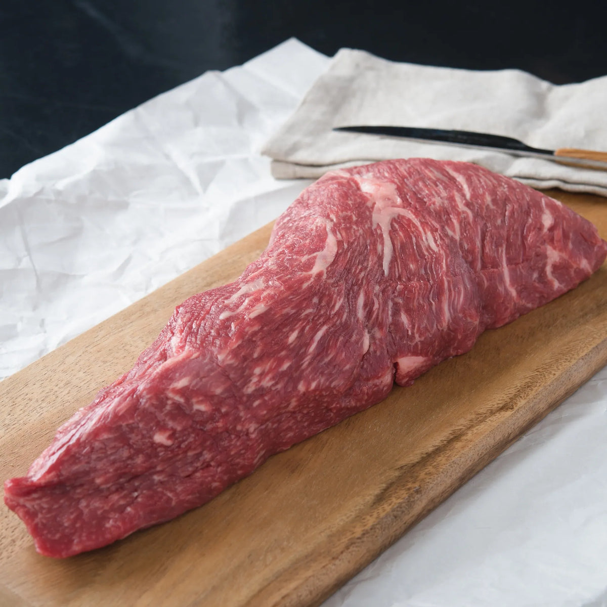 Australian Wagyu Halal Tri Tip Roast, a marbled steak on a wooden board, showcases its rich texture, ideal for grilling or roasting.