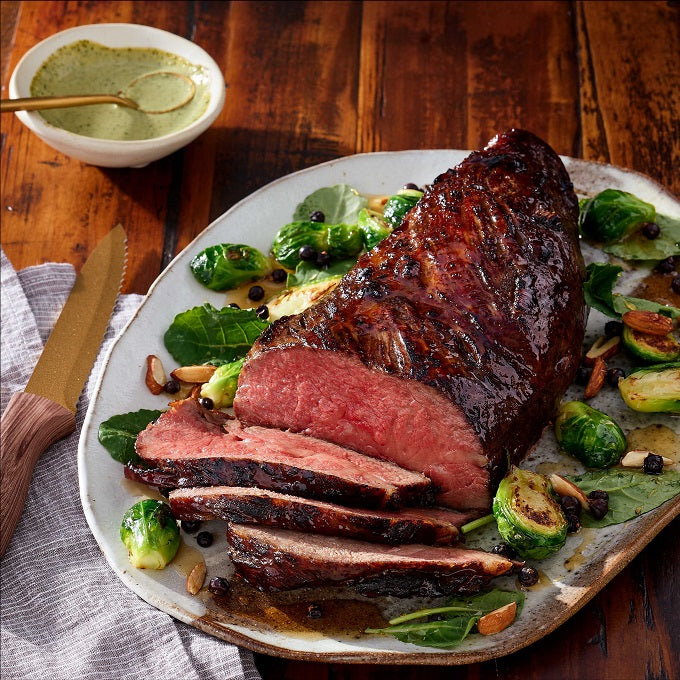 Australian Wagyu Halal Tri Tip Roast, medium-rare, on greens with Brussels sprouts, peppercorns, and almonds. Served with creamy green sauce on the side.