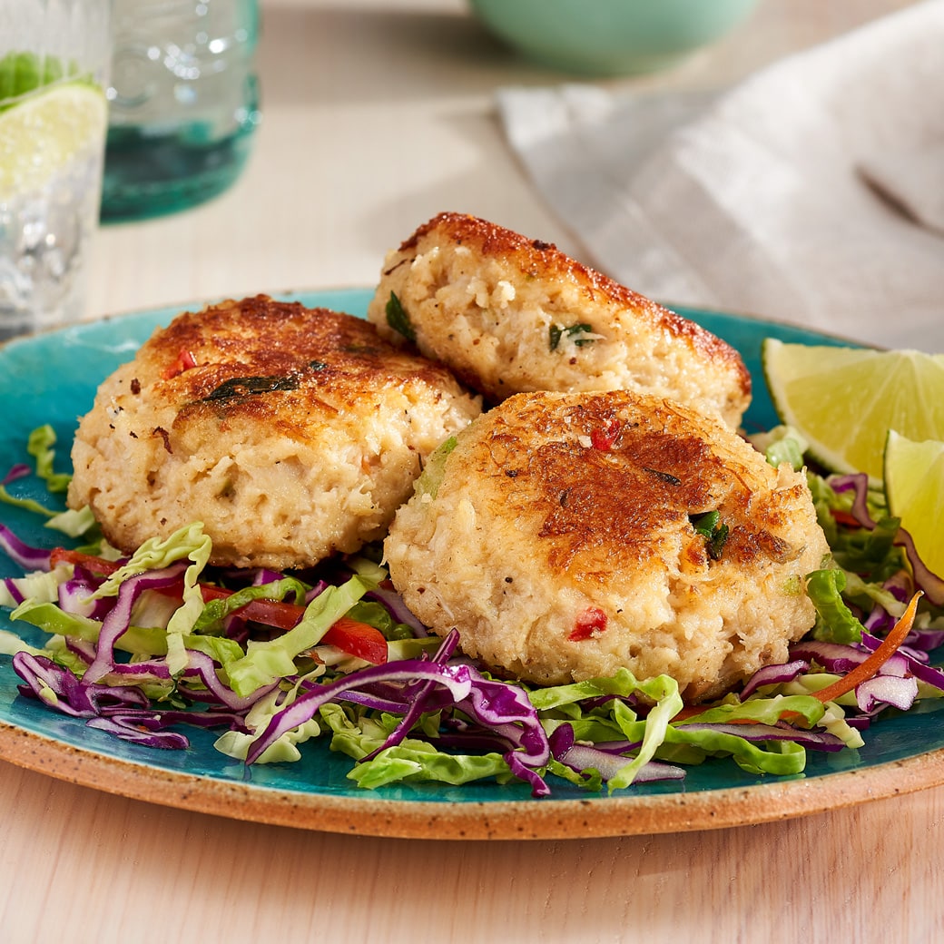 Key West Crab Cakes atop shredded cabbage, garnished with lime wedges, highlighting their fresh, sustainably harvested crab meat and unique seasoning blend.