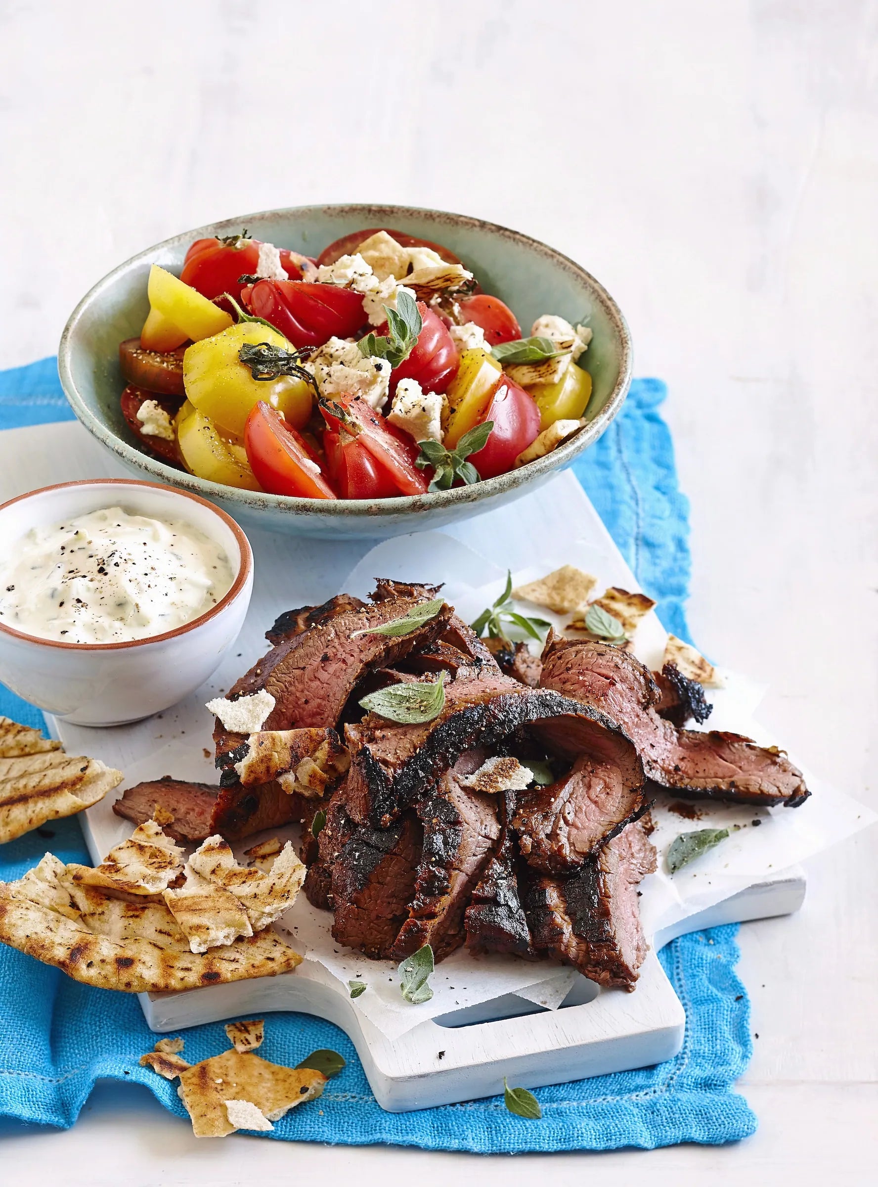 Plated dish with sliced beef, vegetables, and a side of dip on a white background