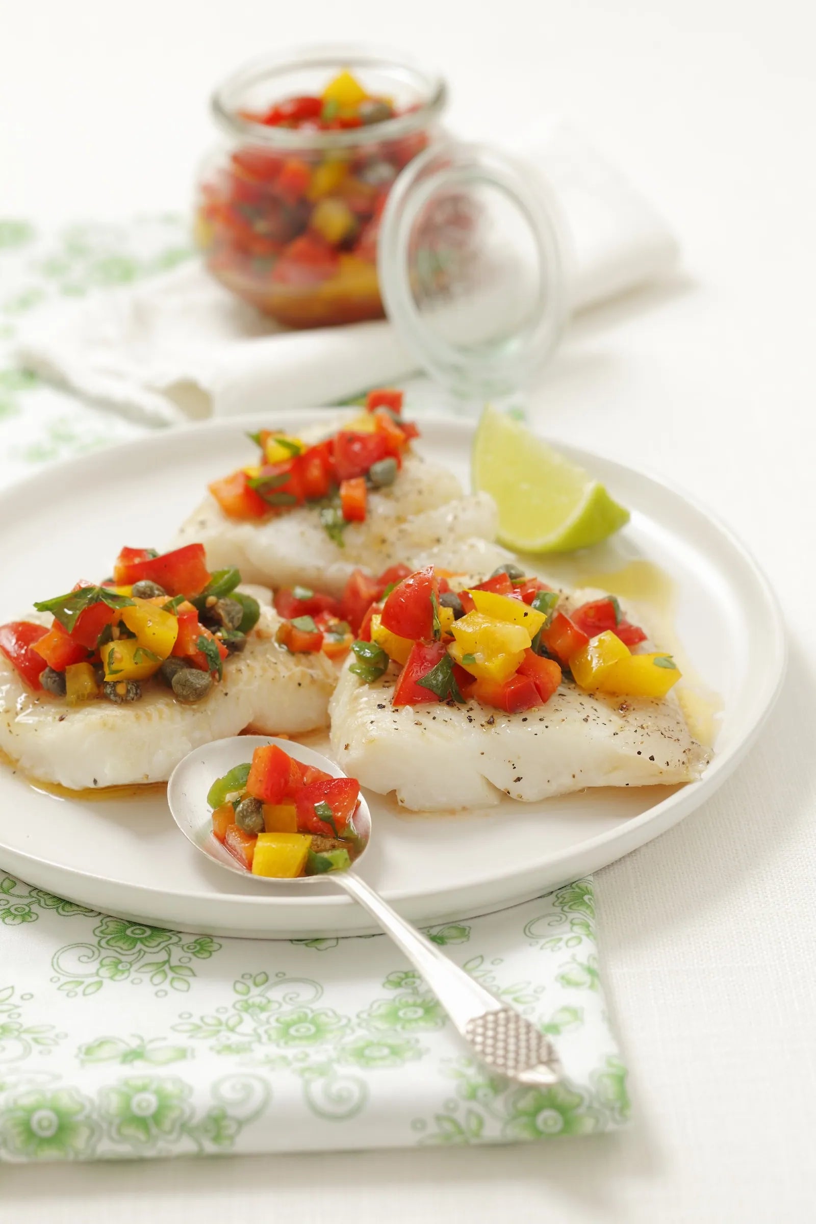 Plated fish with a colorful pepper salsa on a white plate with a green napkin.