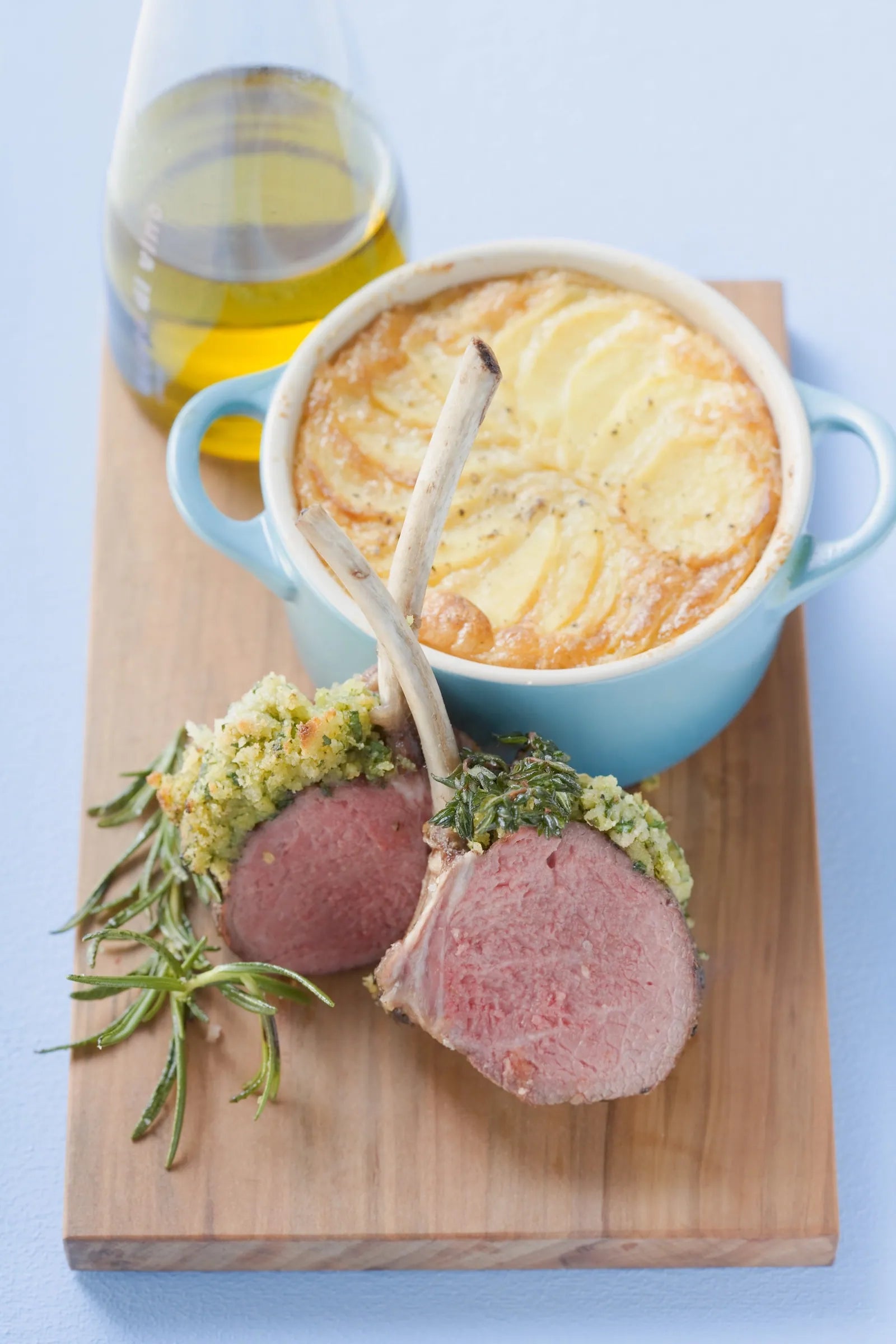 Two lamb chops with rosemary on a wooden board with a dish of mashed potatoes.