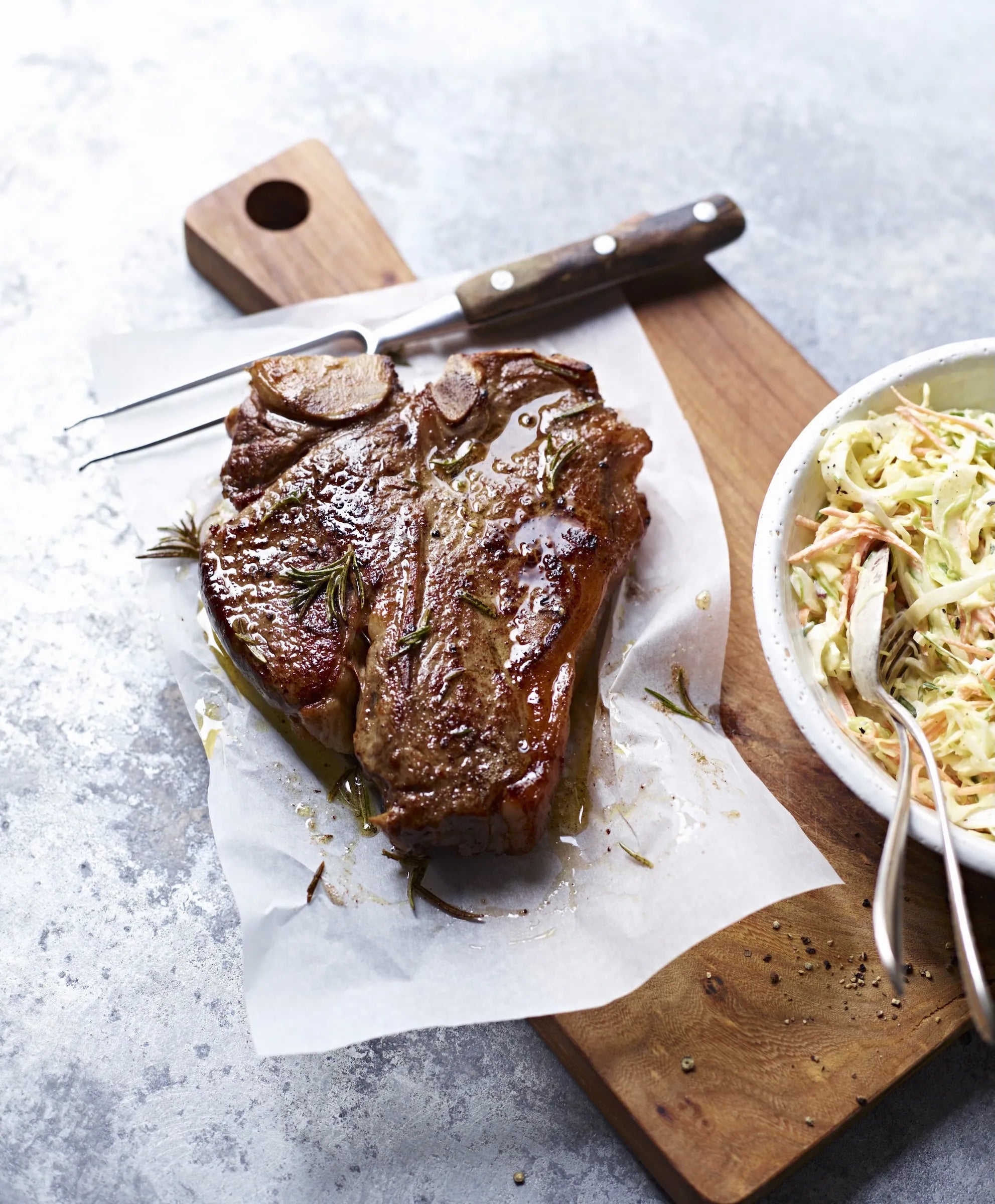 Grilled steak on a wooden cutting board with coleslaw in the background