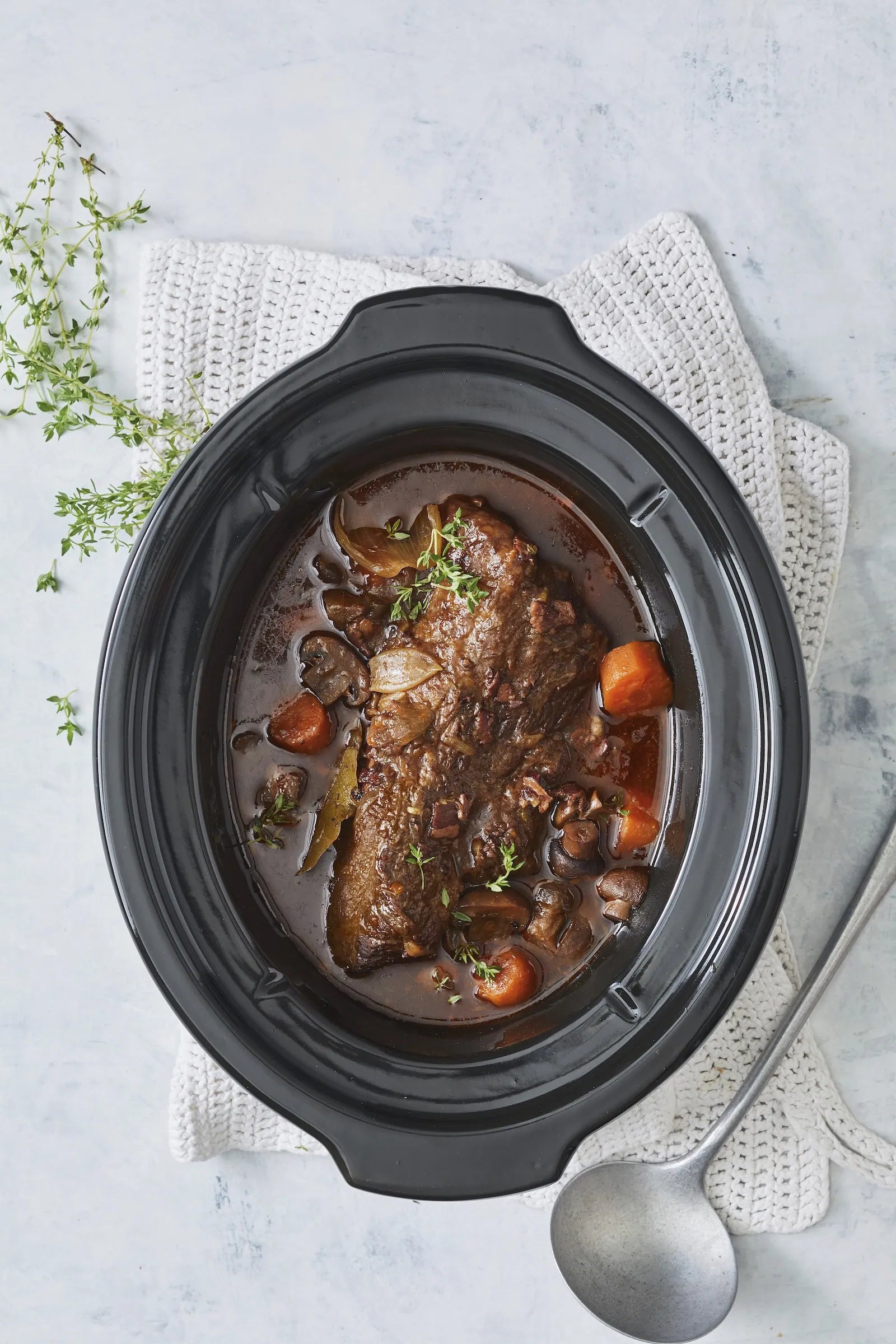 Slow cooker with beef stew on a light gray background