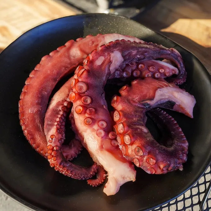 Raw octopus tentacles on a black plate with a blurred background
